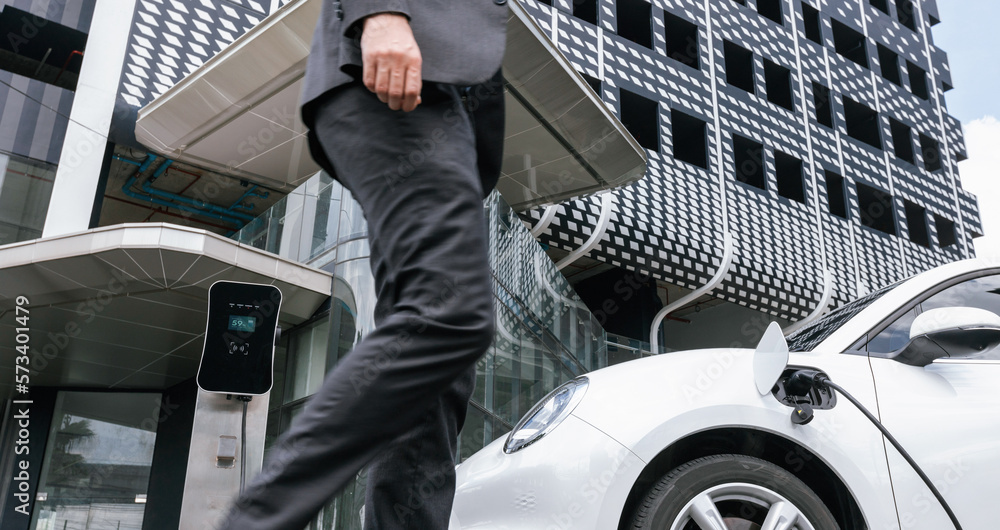 Closeup progressive businessman with electric car recharging at public charging station with backgro