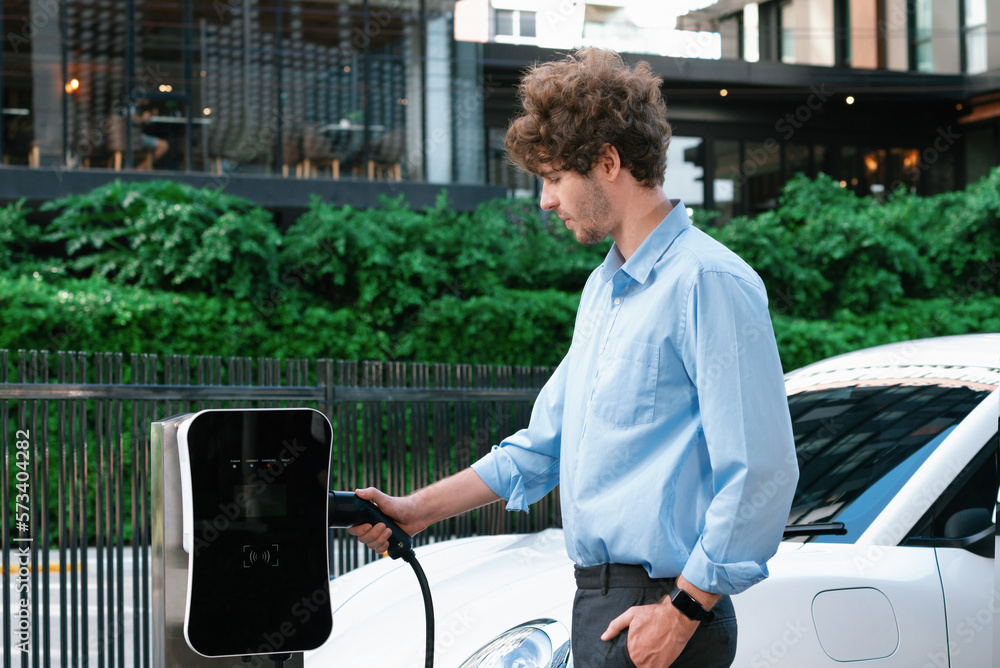 Progressive businessman insert charger plug from charging station to his electric vehicle with apart