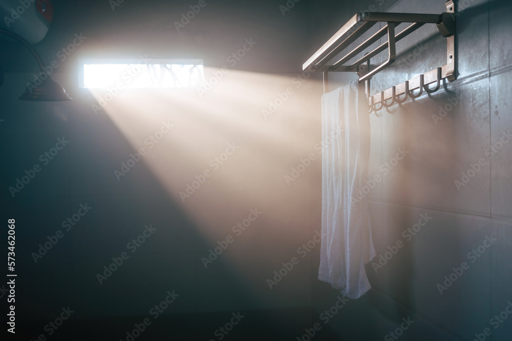 A white towel hangs from a silver fixture in a misty bathroom. The morning light breaks through the 