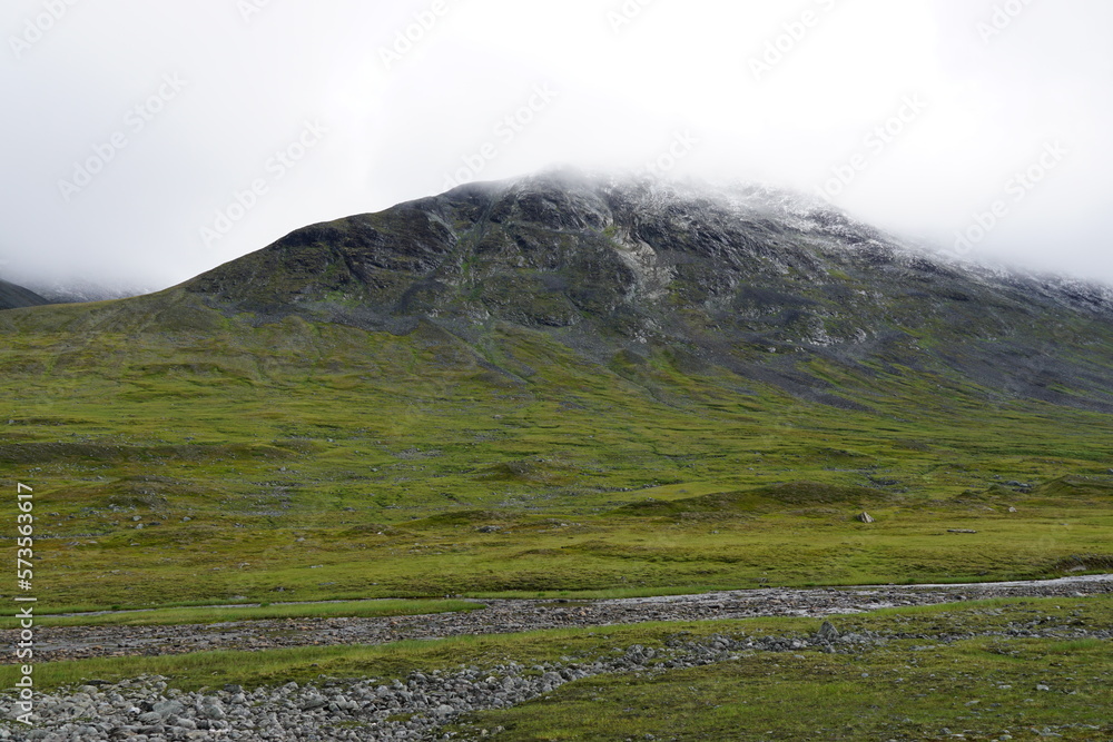 Mountain valley with stream and a peek with snow and clouds in the background