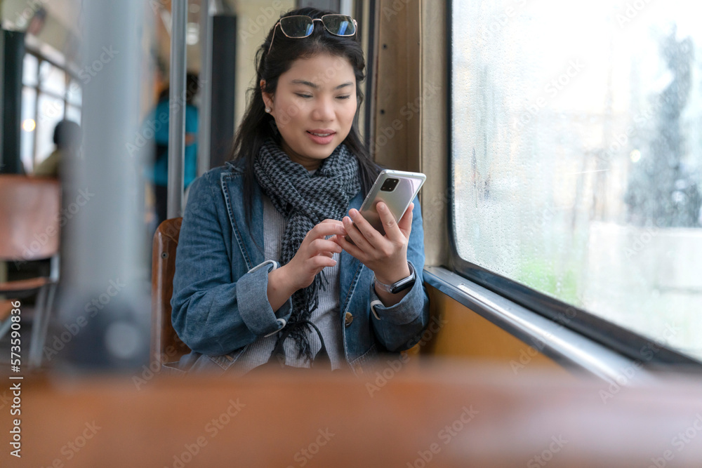 Young and happy asian female woman using smartphone while sitting near the window in the public tran