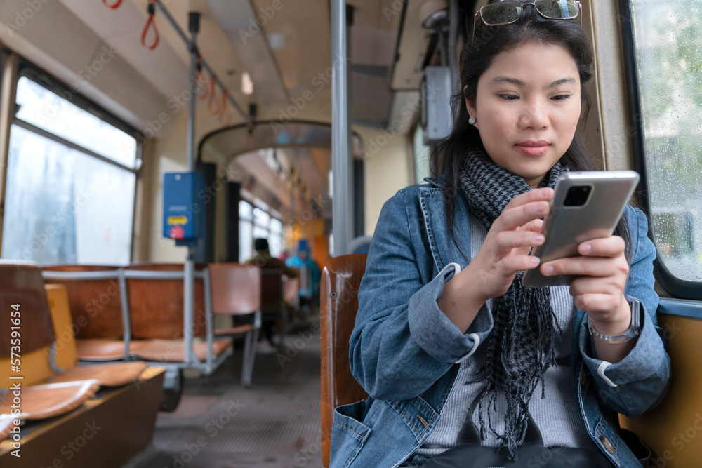 Young and happy asian female woman using smartphone while sitting near the window in the public tran