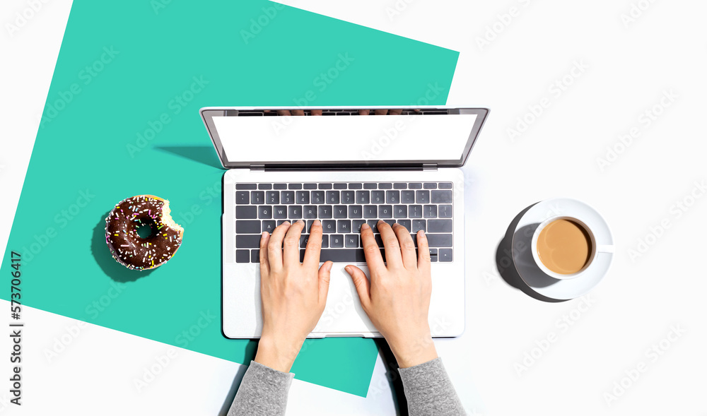 Person using a laptop computer with a donut and a cup of coffee - Flat lay