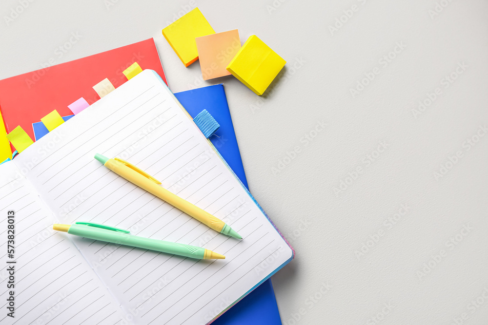 Notebooks, pens and sticky notes on light background, closeup