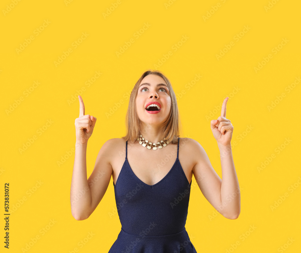 Young woman with necklace pointing at something on yellow background