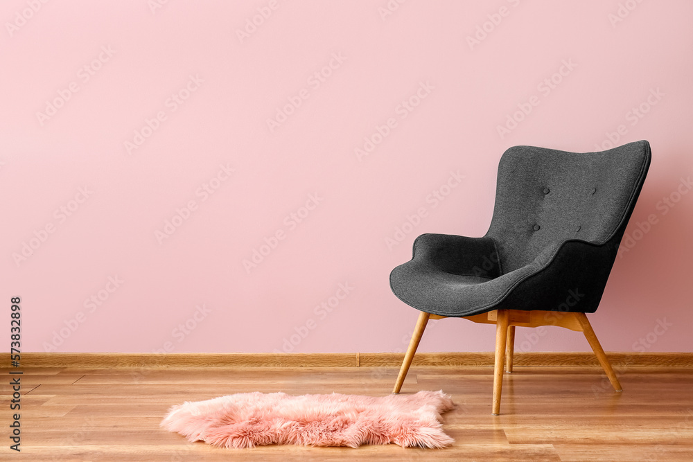 Stylish grey armchair and fur rug near pink wall