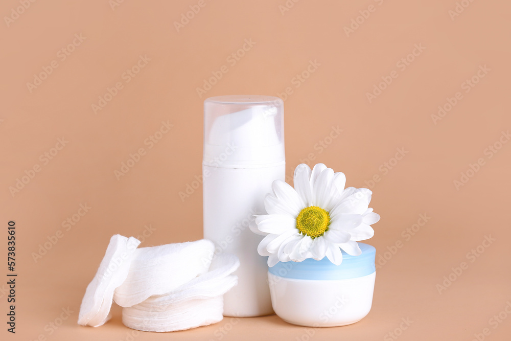 Cosmetic products, cotton pads and chamomile flower on color background