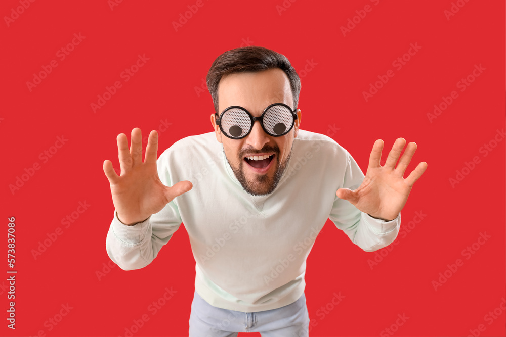 Angry young man in funny eyeglasses on red background. April Fools Day celebration