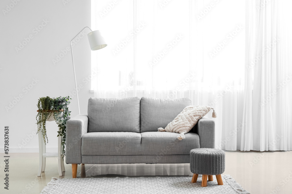 Interior of living room with grey couch, pouf and lamp