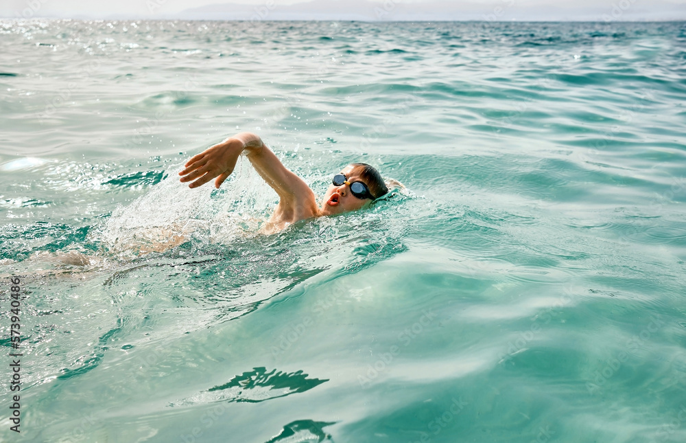 Happy boy in swimming goggles swim in the sea looking at view enjoying summer vacation. Togetherness