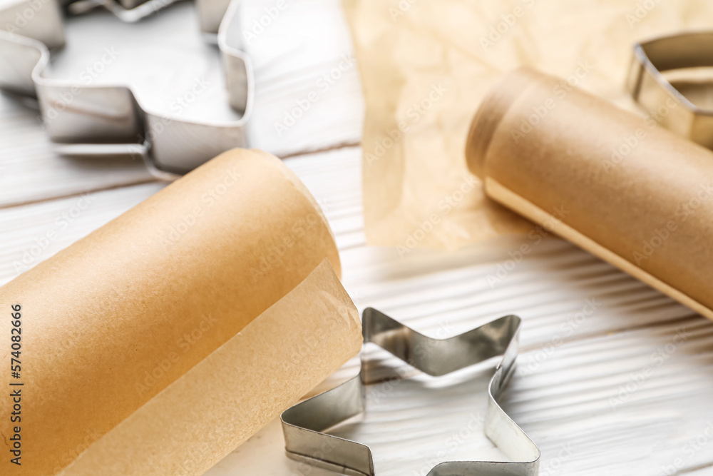 Rolls of baking paper and cookie cutters on light wooden background, closeup