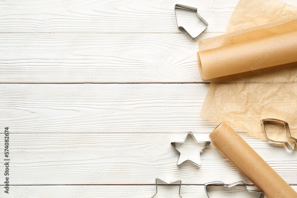 Rolls of baking paper and cookie cutters on light wooden background