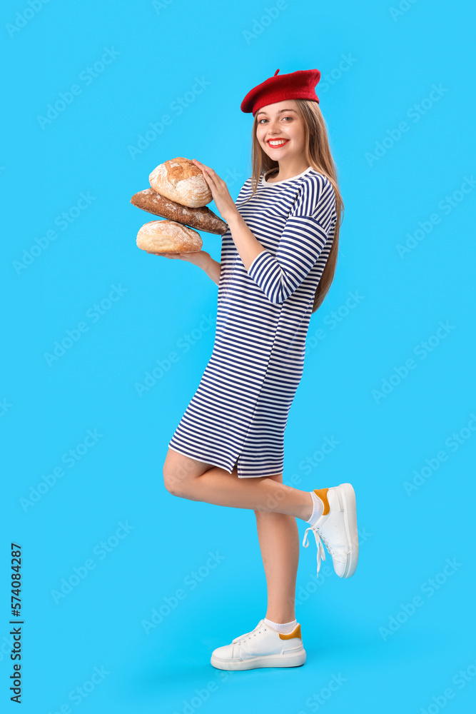 Young woman in beret with loaves of fresh bread on blue background