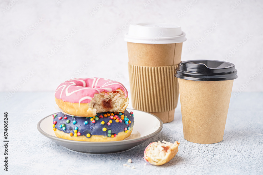 Plate with different delicious donuts and paper cups on white table