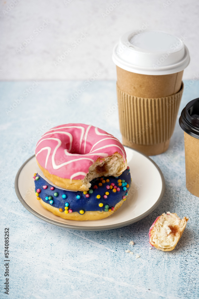 Plate with different delicious donuts and paper cup on white table