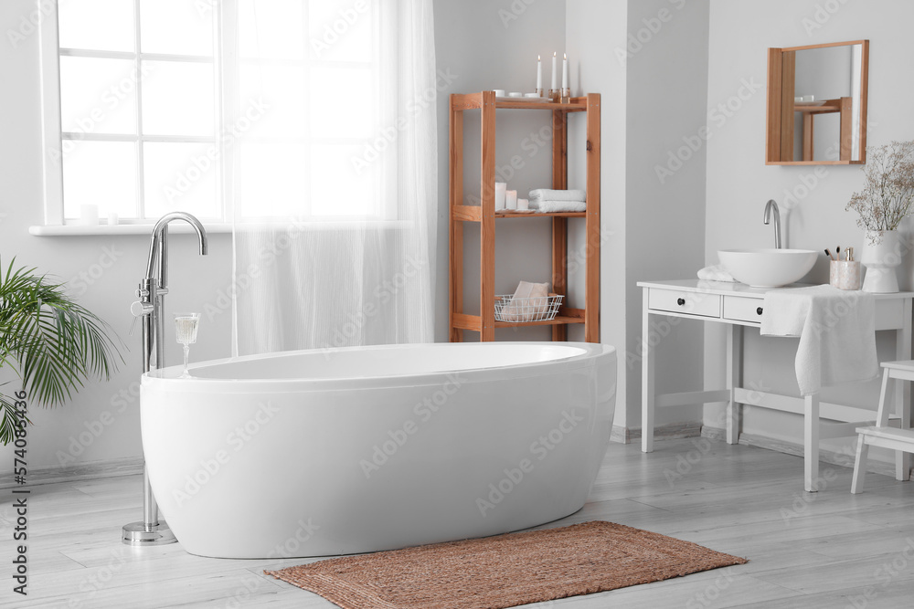 Interior of light bathroom with bathtub, table and sink