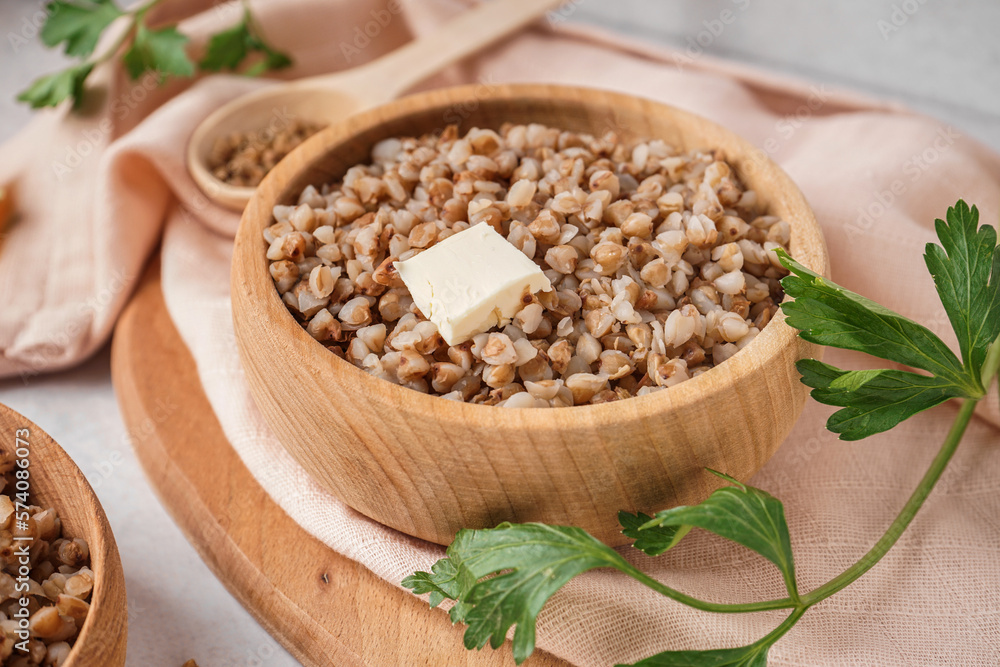 Wooden bowl of tasty buckwheat porridge with butter on grey table