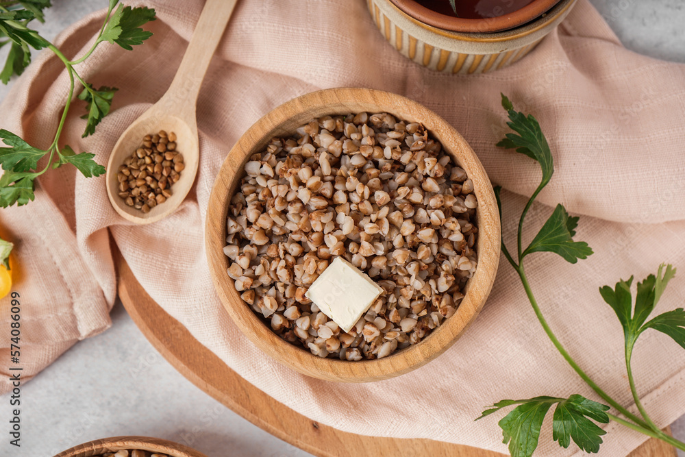 Wooden bowl of tasty buckwheat porridge with butter on grey table