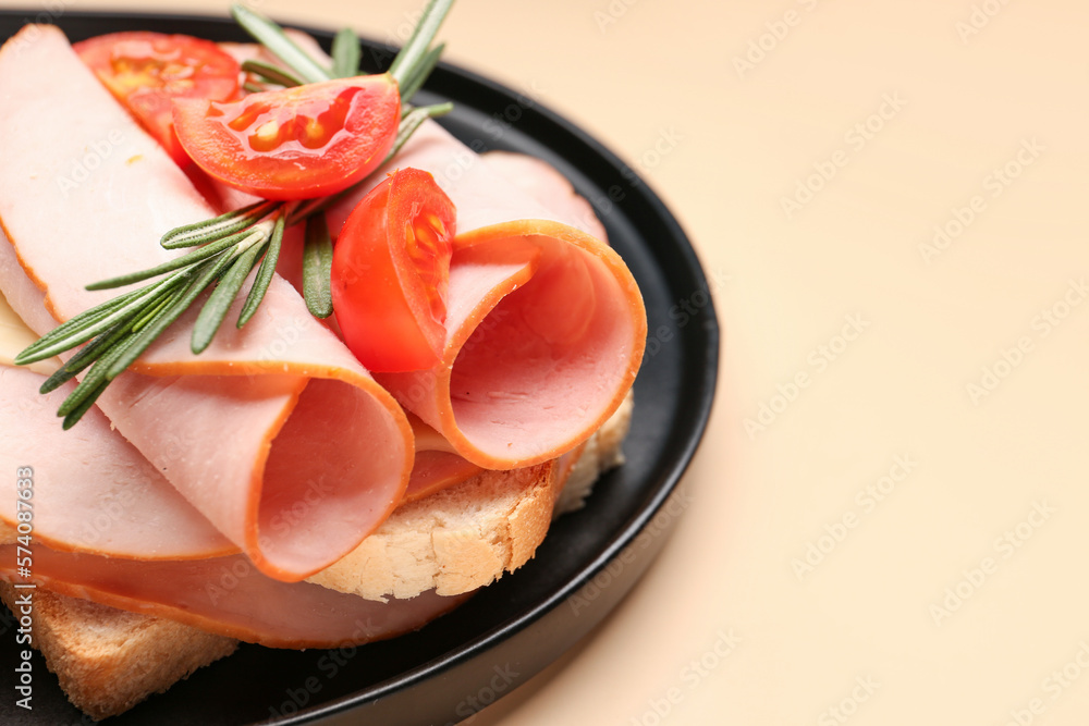 Black board with slices of tasty ham, tomatoes and rosemary on beige background