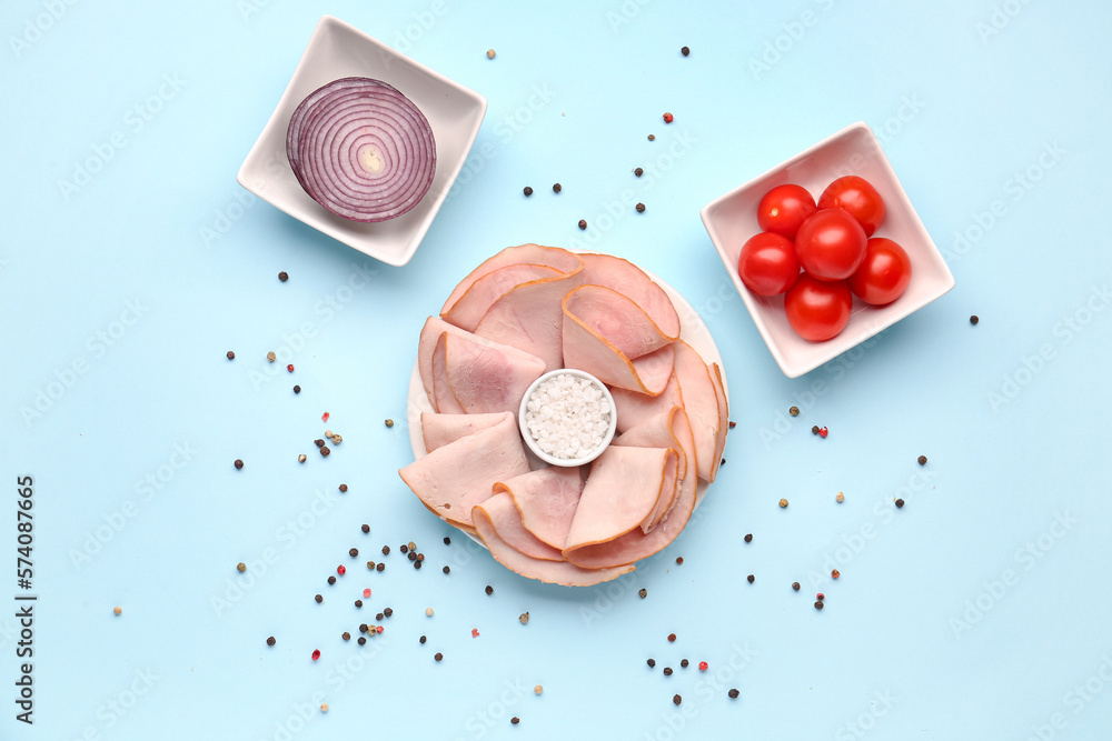 Dishes with slices of tasty ham, sea salt, onion and tomatoes on blue background