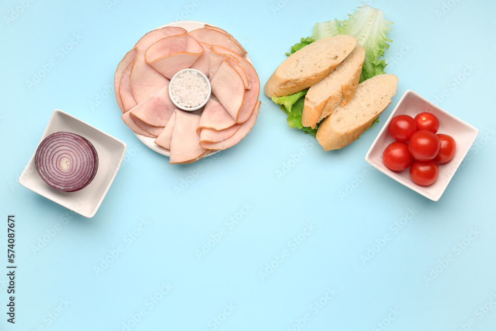 Plate and bowls with ingredients for ham sandwich on blue background