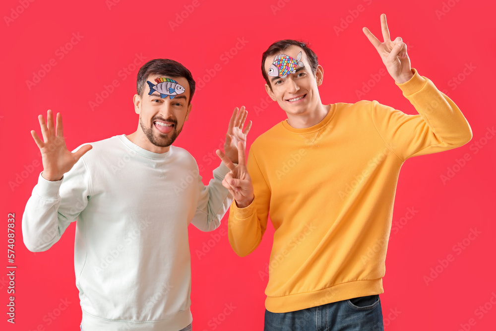 Young men with paper fishes on red background. April Fools Day celebration