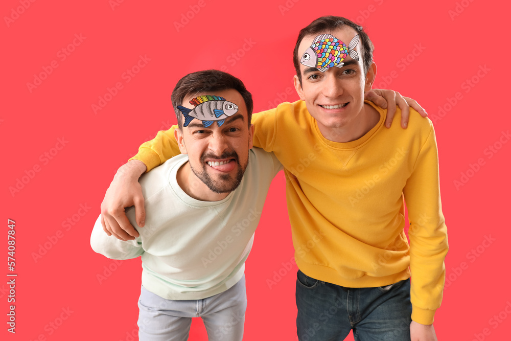 Young men with paper fishes on red background. April Fools Day celebration