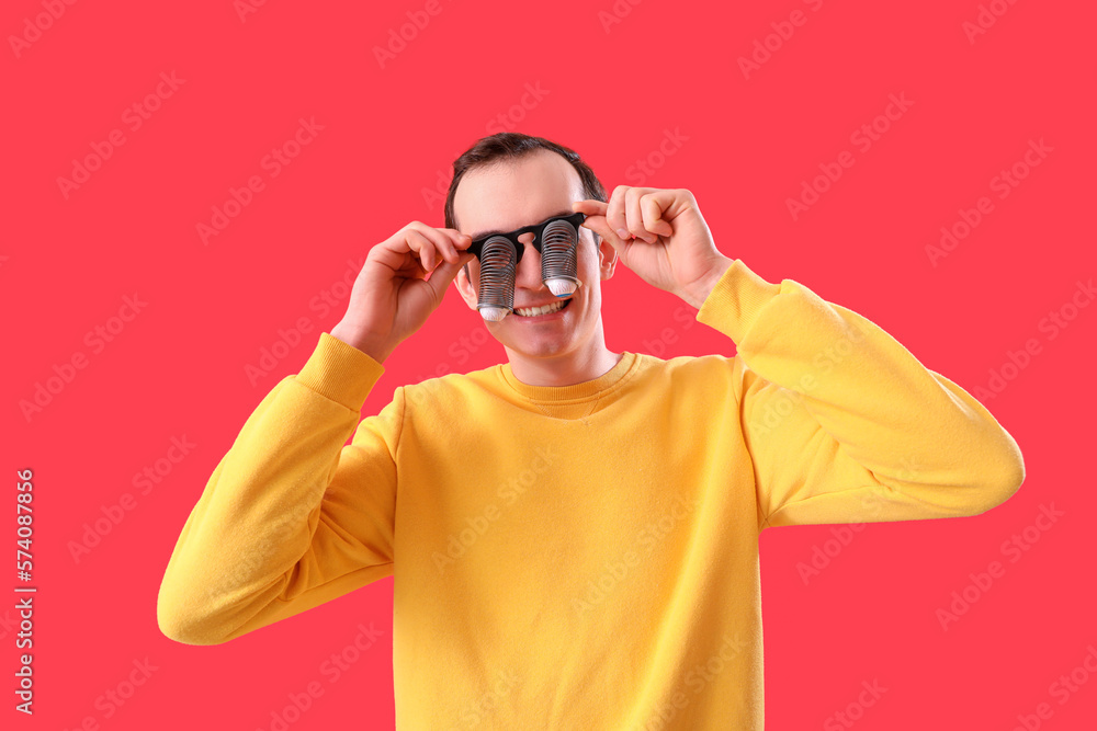 Young man in funny eyeglasses on red background. April Fools Day celebration