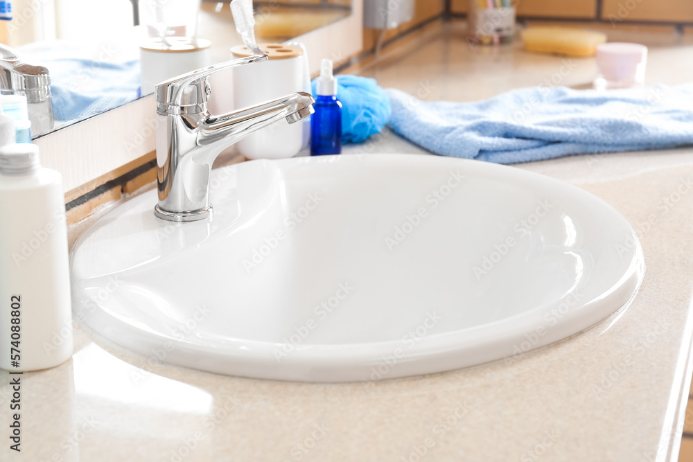 Table with white ceramic sink and bath supplies in room, closeup