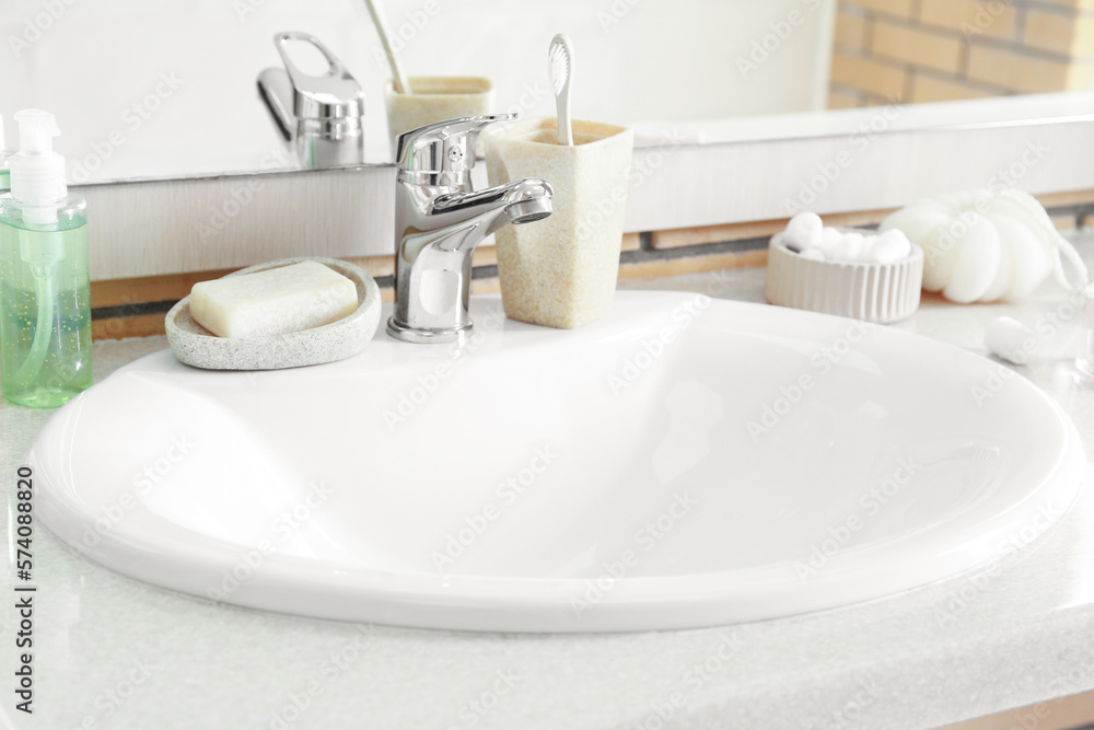 Table with white ceramic sink and bath supplies in room, closeup