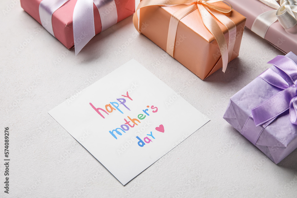 Card with text HAPPY MOTHERS DAY and gift boxes on light background, closeup