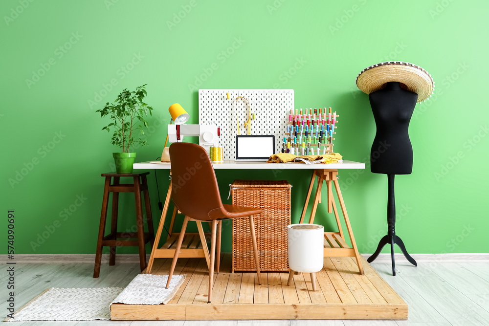 Tailors workplace with laptop, sewing machine and organizers near green wall in workshop