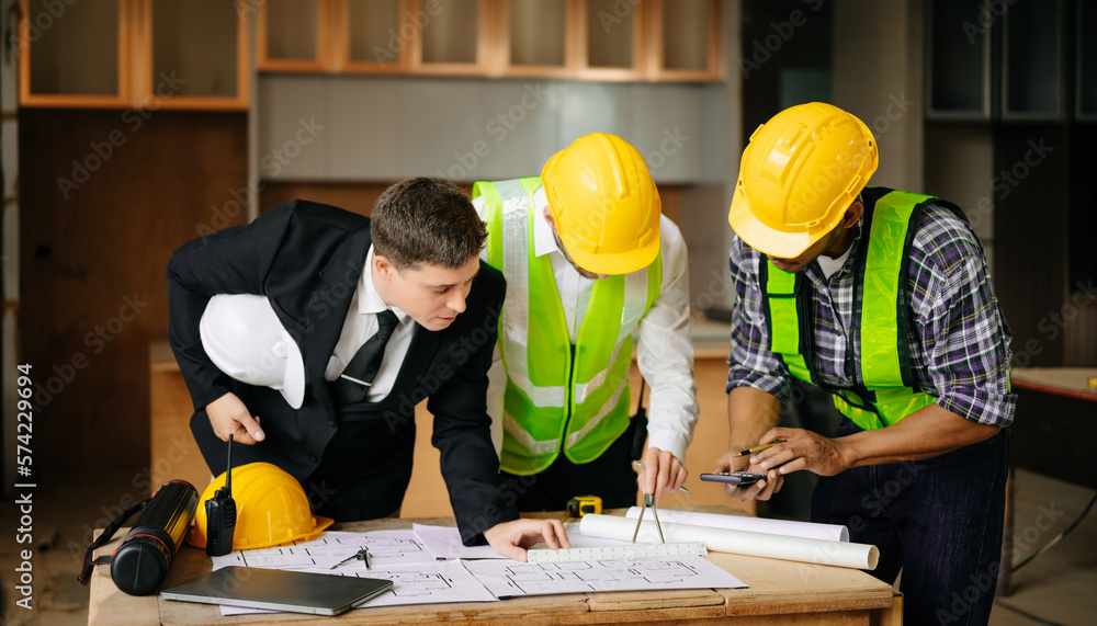 Contractor and architect looking at plan, tablet, laptop and talking about working on big project. B