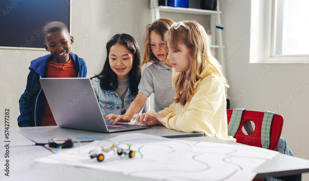 Kids working together to program a robot car with a laptop in a computer science class