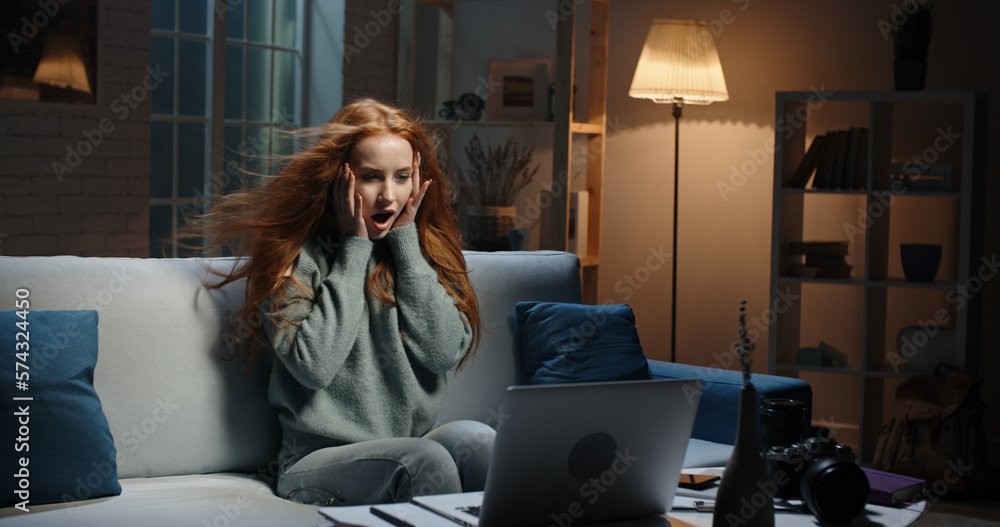 Pretty caucasian redhead girl looking at laptop screen, hair blowing, reading breaking news, seeing 