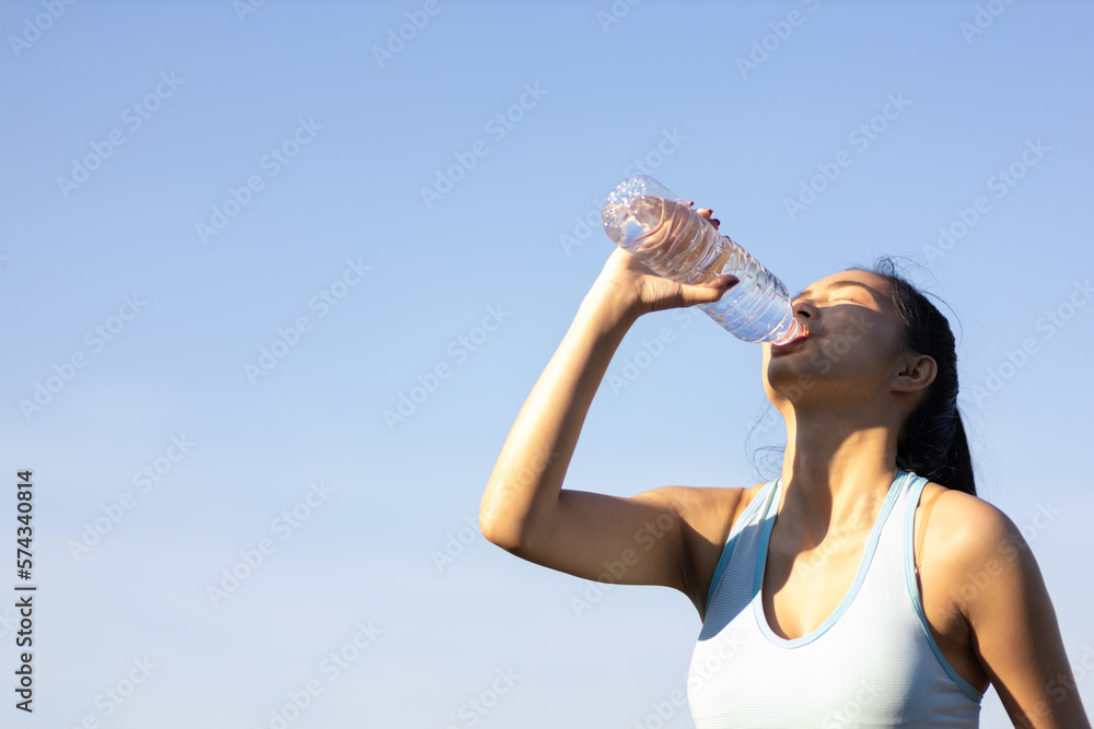 Thirsty Asian female athlete drinking water after exercising outdoors in park.