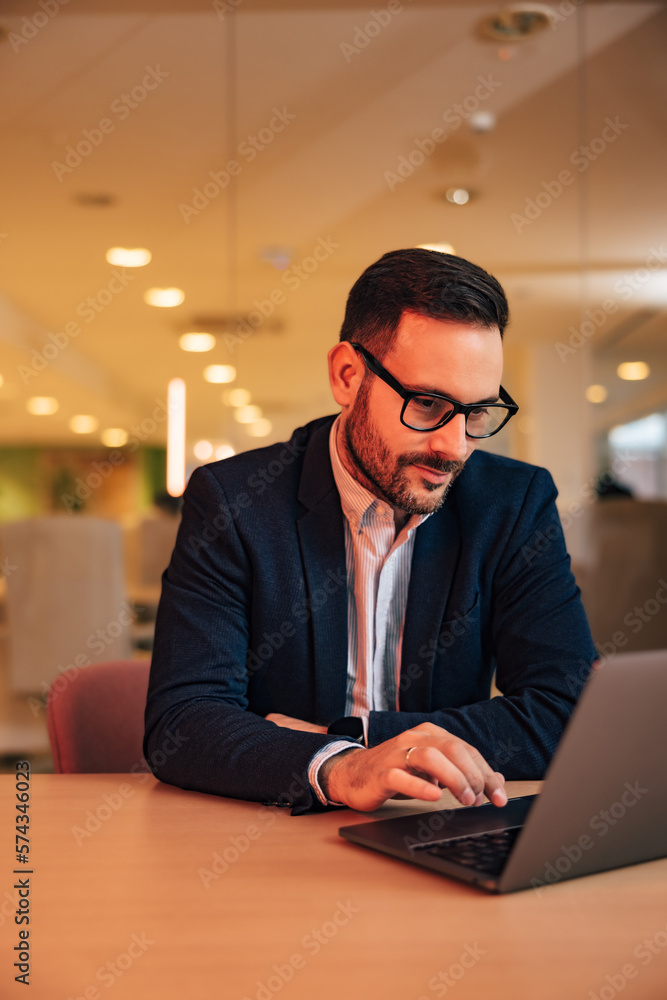 Serious businessman working over the laptop, sitting at the office, elegantly dressed.