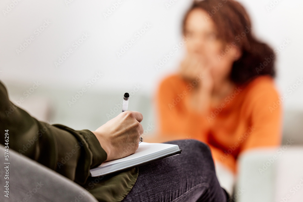 Close-up of a female psychologist sitting with a patient, holding a pen while making notes.