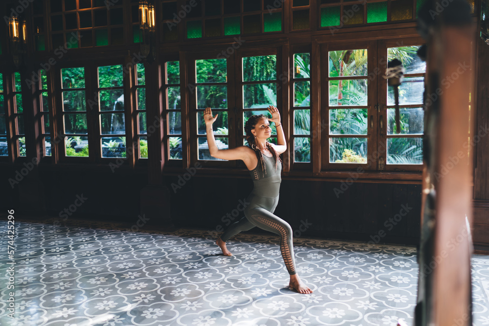 Slim woman doing warrior pose and practicing yoga in spacious hall