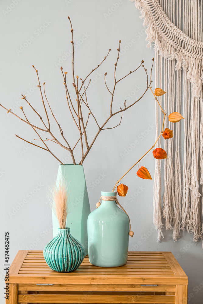 Vases with tree branches on wooden table near light wall