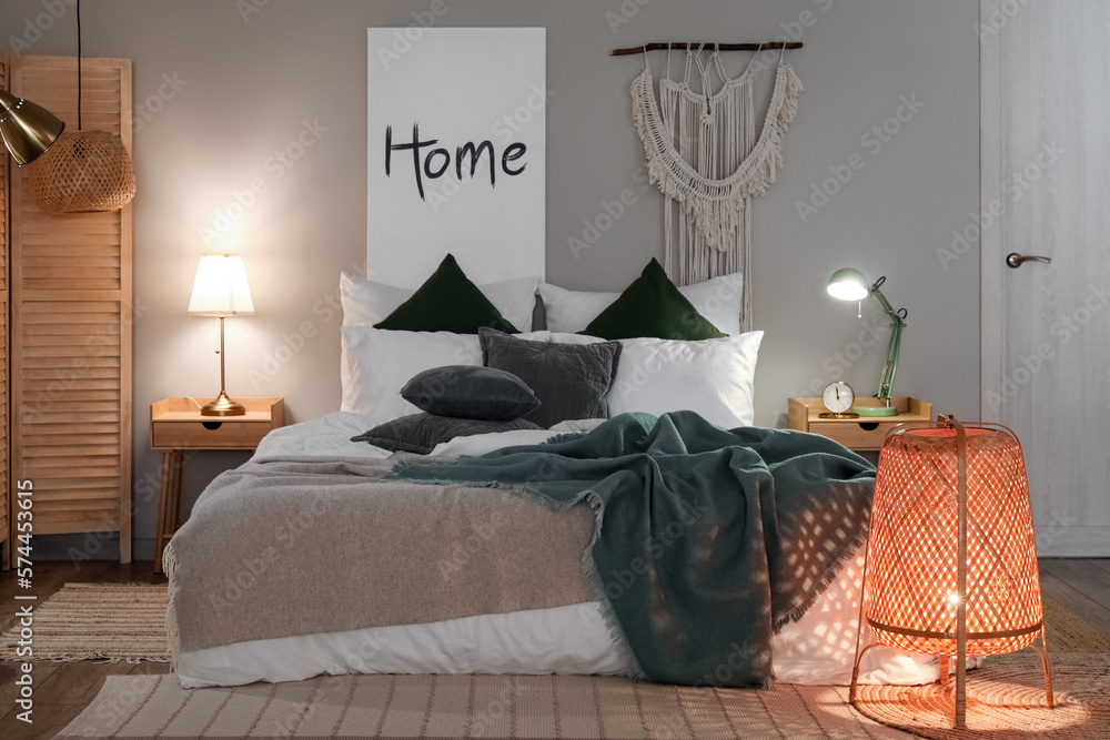 Interior of bedroom with green blankets on bed and glowing lamps late in evening