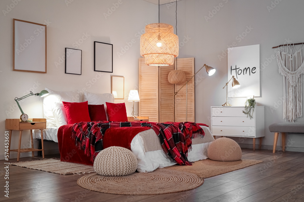 Interior of bedroom with red checkered blankets on bed and glowing lamps late in evening