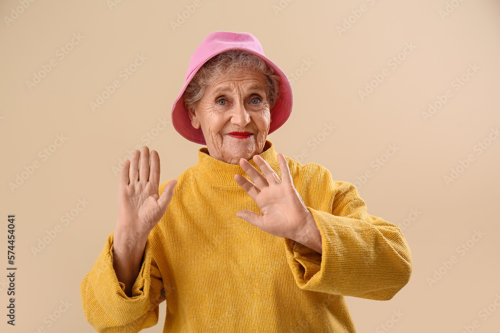 Senior woman in bucket hat on beige background