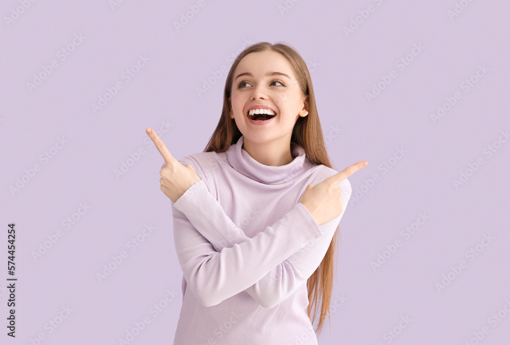 Happy young woman in sweater pointing at something on lilac background