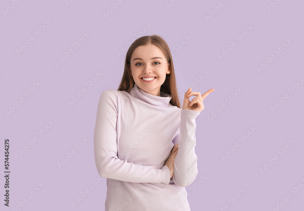 Young woman in sweater pointing at something on lilac background