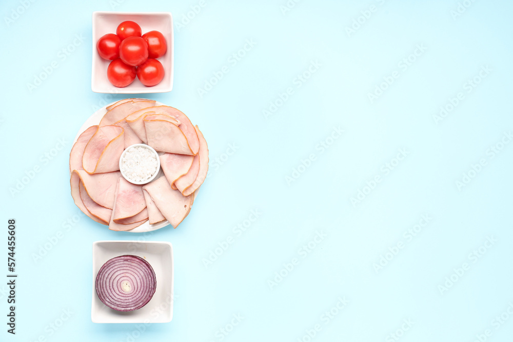 Dishes with slices of tasty ham, sea salt, onion and tomatoes on blue background