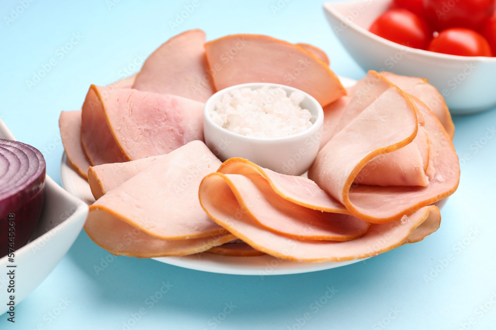 Dishes with slices of tasty ham, sea salt and tomatoes on blue background