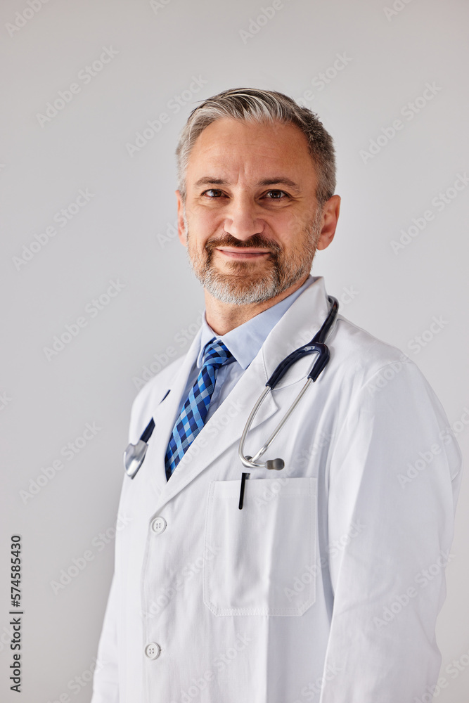 Portrait of a smiling male doctor, with a stethoscope, standing in front of the grey wall.