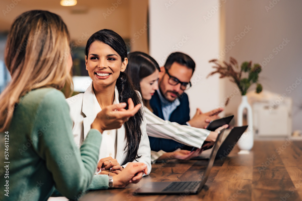 Smiling businesswoman talking with a female colleague, taking a work break, sitting at the office.