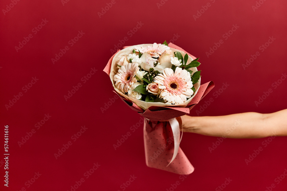 Photo of a crossed arm, holding a bouquet of flowers wrapped in pink paper.